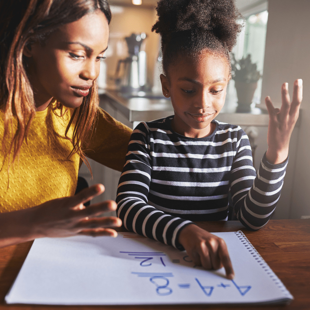 A parent helping their child to complete Maths homework while the child writes sums on a white board.